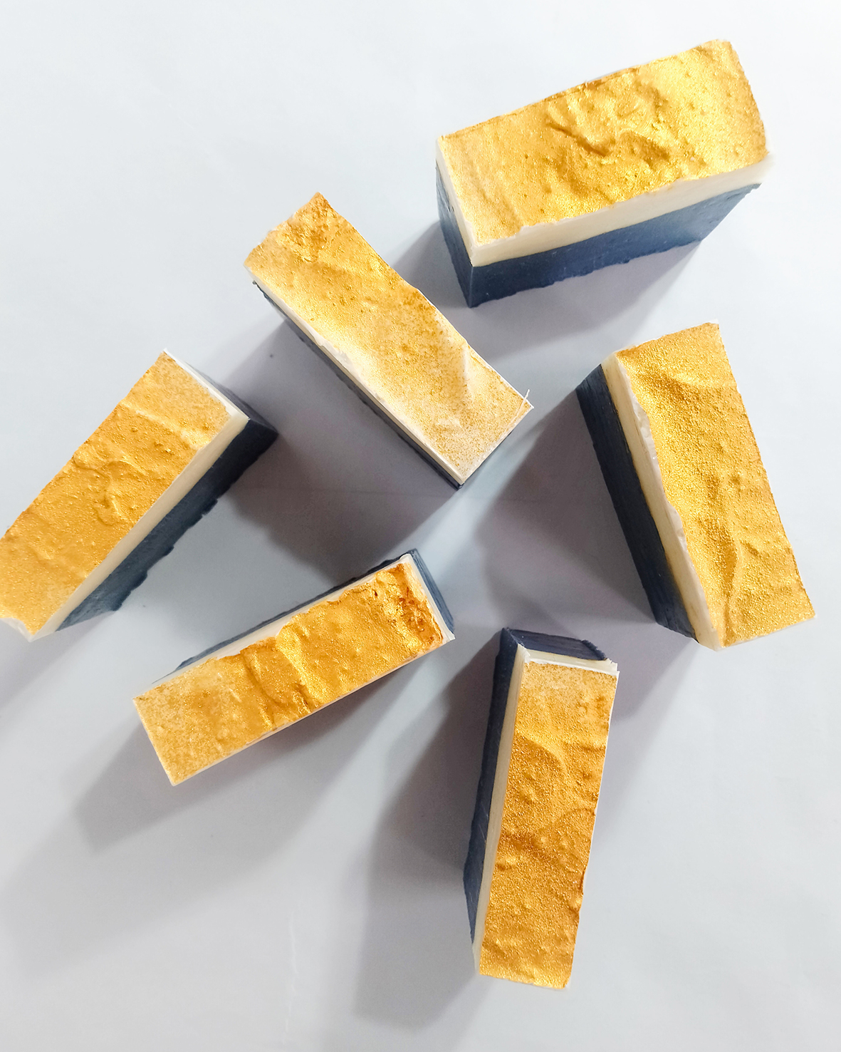 Sapone bicolore con lattato di sodio su sfondo bianco, diverse saponette in piedi e fotografate dall’alto.